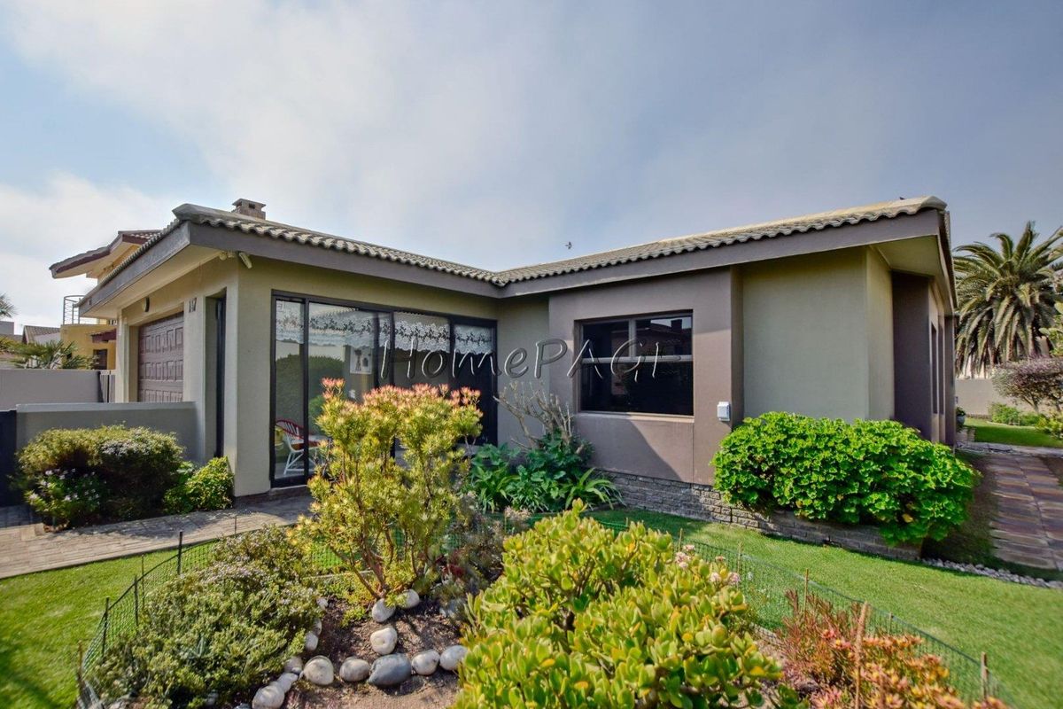 A well-maintained rear exterior view of the house featuring a paved walkway, landscaped garden, stone cladding accents, and sliding glass doors.
