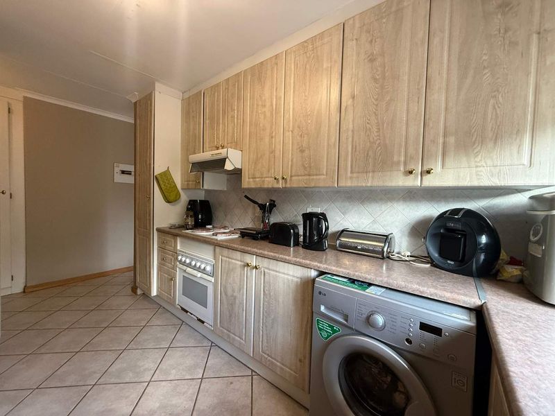 A functional kitchen featuring light wood-finish cabinetry, laminate countertops, a built-in oven with extractor fan, and tiled flooring.