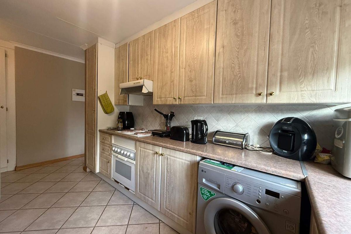 A functional kitchen featuring light wood-finish cabinetry, laminate countertops, a built-in oven with extractor fan, and tiled flooring.