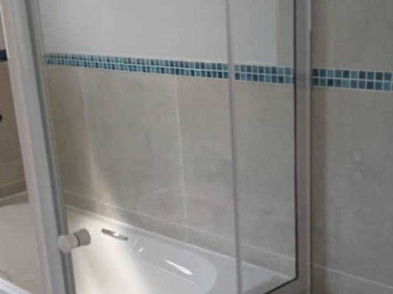A functional bathroom featuring a built-in bathtub, glass shower screen, and neutral wall tiling with a decorative mosaic accent border.