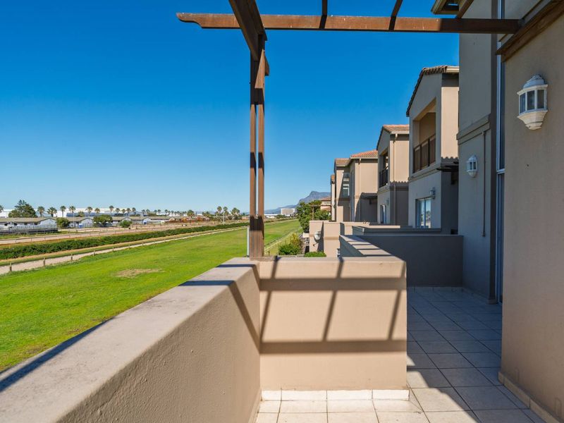 Spacious balcony featuring tiled flooring, a timber pergola, and wall-mounted lighting, offering expansive views over the adjacent green space.