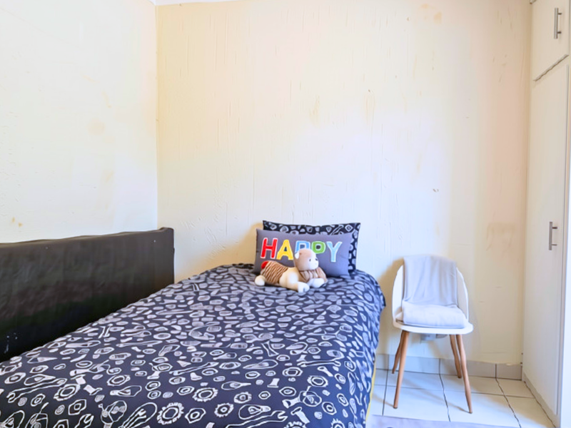 A compact bedroom featuring tiled flooring and a built-in wardrobe, currently showing signs of wear on the wall surfaces.