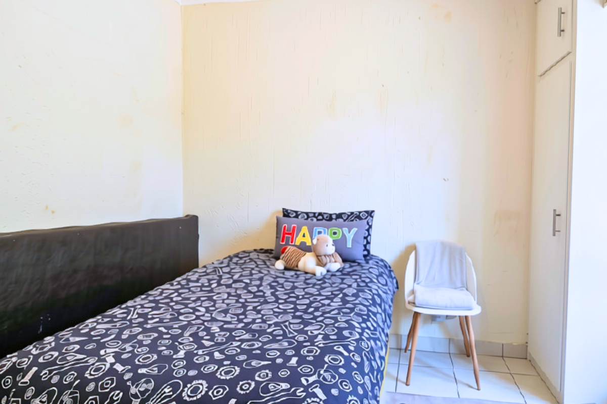 A compact bedroom featuring tiled flooring and a built-in wardrobe, currently showing signs of wear on the wall surfaces.