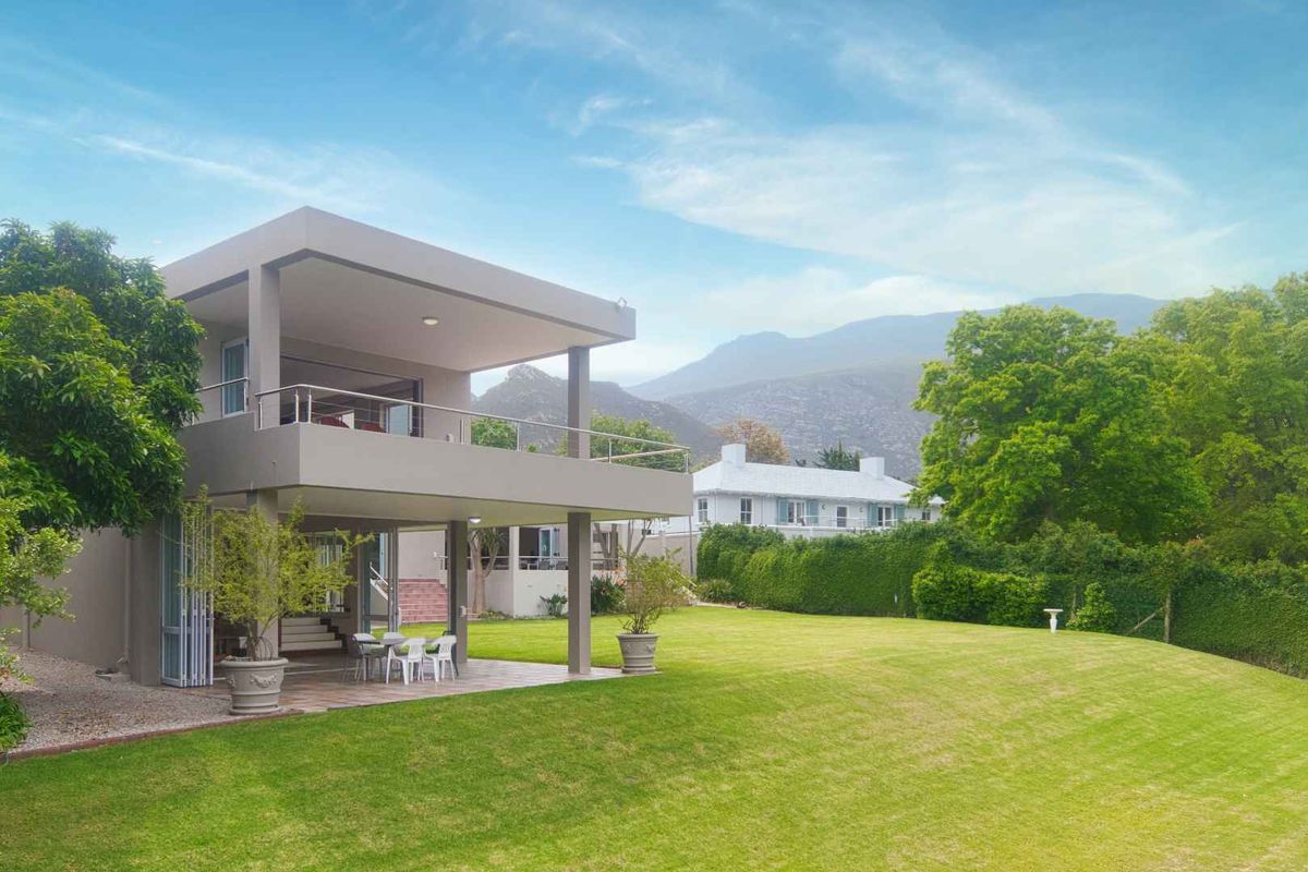 Rear view of the property featuring a spacious lawn, a covered ground-floor patio, and an upper-level balcony with mountain views.