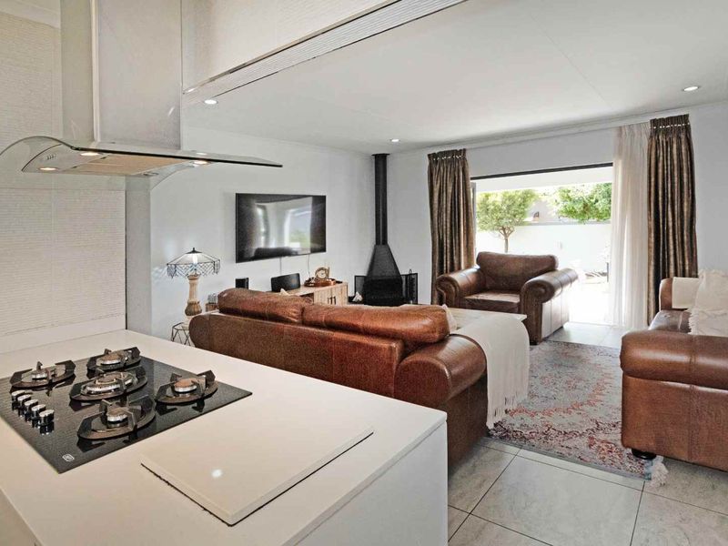 Open-plan living area featuring a modern kitchen with gas hob and extractor, flowing into a lounge with a fireplace and access to the patio.