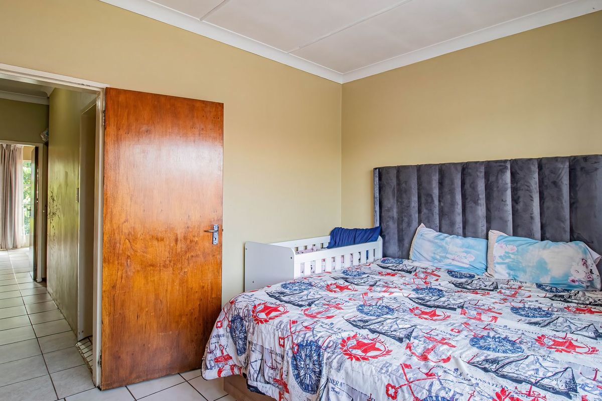 A bedroom featuring neutral wall tones, a solid wood door, and cove cornicing, with an adjacent hallway visible through the doorway.