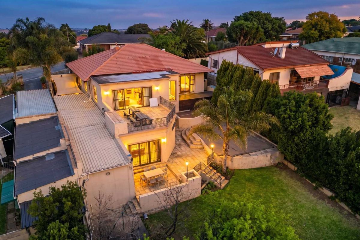 Aerial view of a multi-level residential property featuring a tiled roof, spacious rear terraces, paved patio areas, and a well-maintained garden.