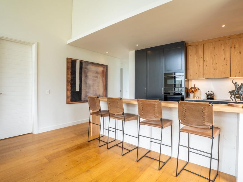 Modern open-plan kitchen featuring high-end cabinetry, a stone breakfast bar, and warm timber flooring, creating a seamless and sophisticated living space.
