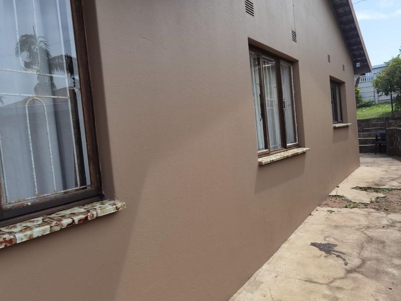Side view of the house exterior featuring painted walls, security bars on windows, tiled sills, and a concrete pathway leading to the rear garden.