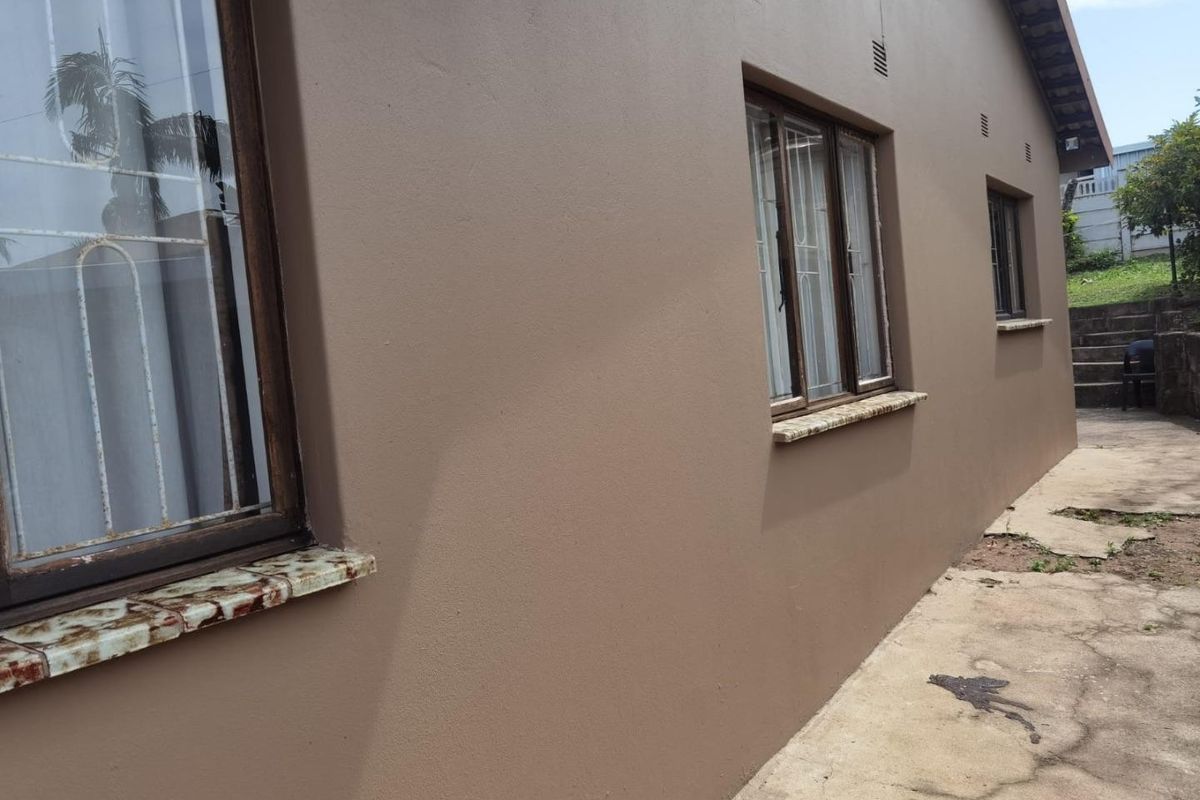 Side view of the house exterior featuring painted walls, security bars on windows, tiled sills, and a concrete pathway leading to the rear garden.