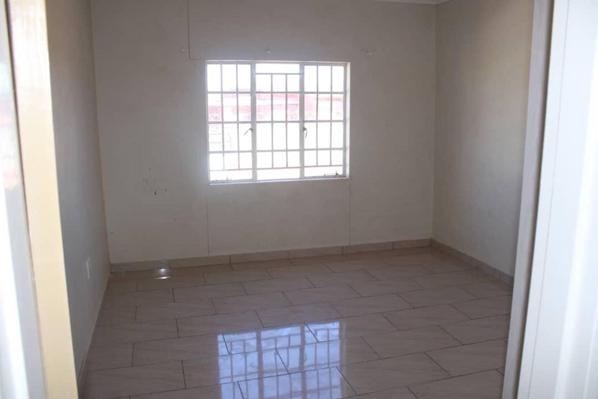 An empty bedroom featuring tiled flooring and a window fitted with security burglar bars.