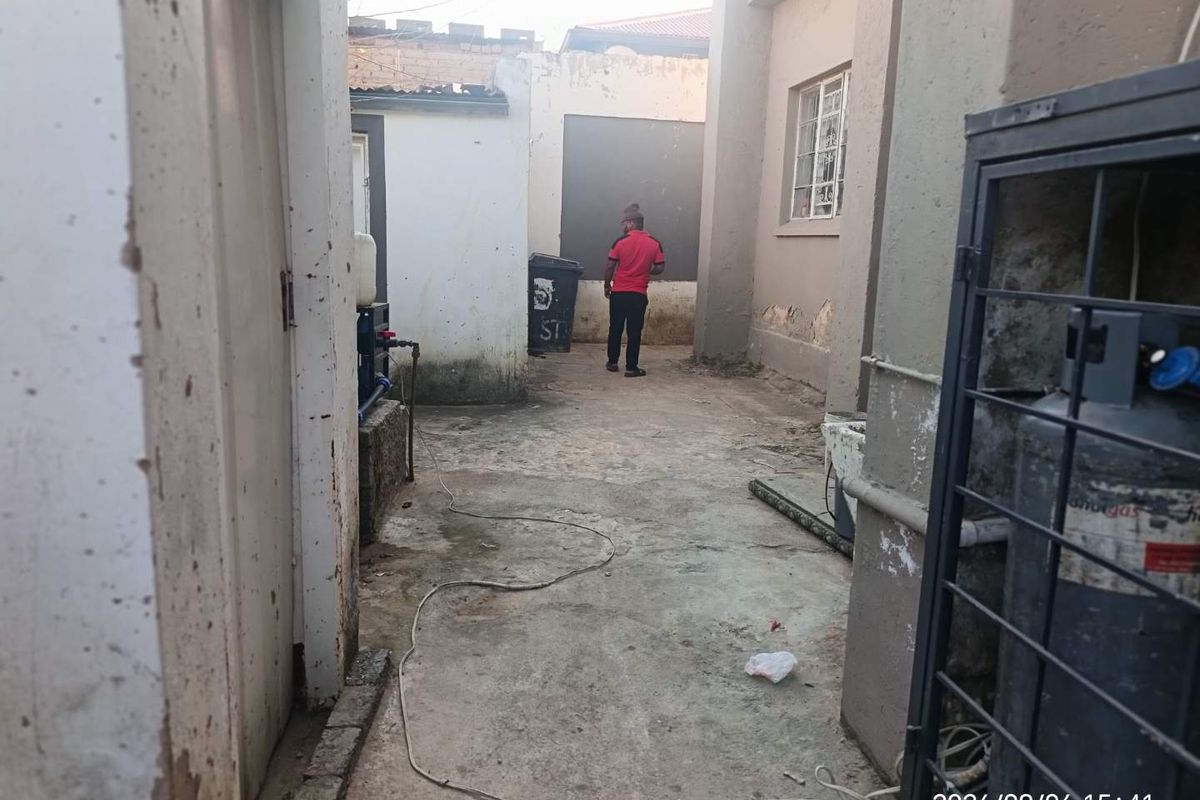A narrow rear exterior service area featuring concrete paving and visible wear to the building's exterior wall plaster and paint finishes.