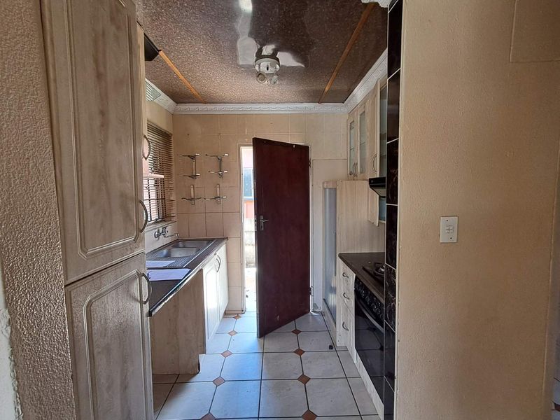 A compact kitchen featuring built-in cabinetry, a built-in oven, and tiled flooring, offering a functional layout with direct access to the exterior.