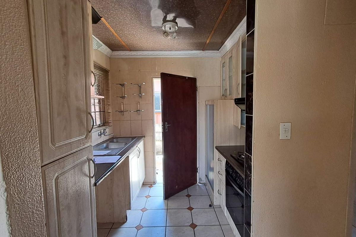 A compact kitchen featuring built-in cabinetry, a built-in oven, and tiled flooring, offering a functional layout with direct access to the exterior.