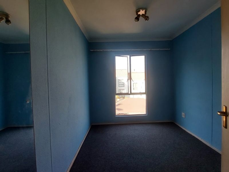 An empty bedroom featuring blue walls, carpeted flooring, a built-in cupboard, and a window providing natural light.