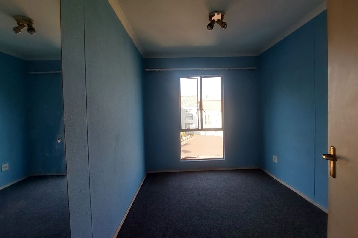 An empty bedroom featuring blue walls, carpeted flooring, a built-in cupboard, and a window providing natural light.