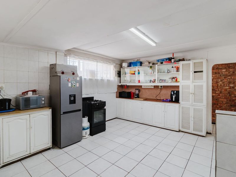 A functional kitchen featuring white cabinetry, tiled flooring, a gas stove, and an exposed brick accent wall, offering potential for modern renovation.
