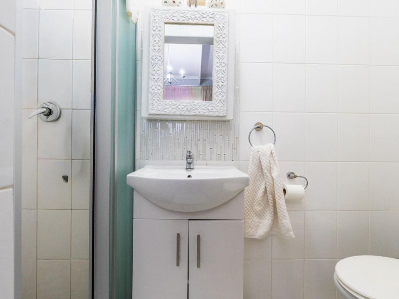 A compact bathroom featuring a white vanity cabinet, ceramic basin, wall-mounted mirror, and tiled wall finishes.