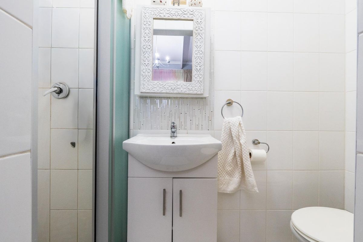 A compact bathroom featuring a white vanity cabinet, ceramic basin, wall-mounted mirror, and tiled wall finishes.