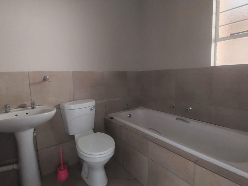 A functional bathroom featuring a pedestal basin, toilet, and a built-in bathtub with neutral wall tiling.