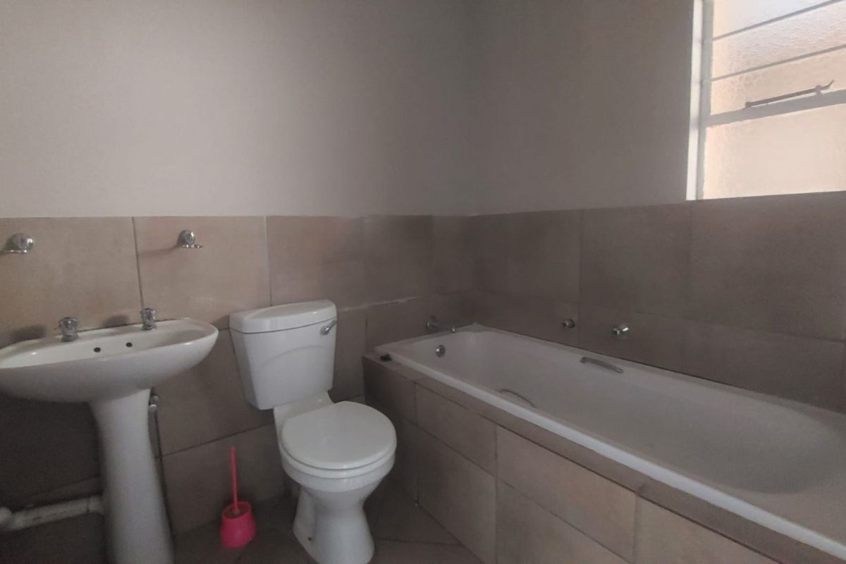A functional bathroom featuring a pedestal basin, toilet, and a built-in bathtub with neutral wall tiling.