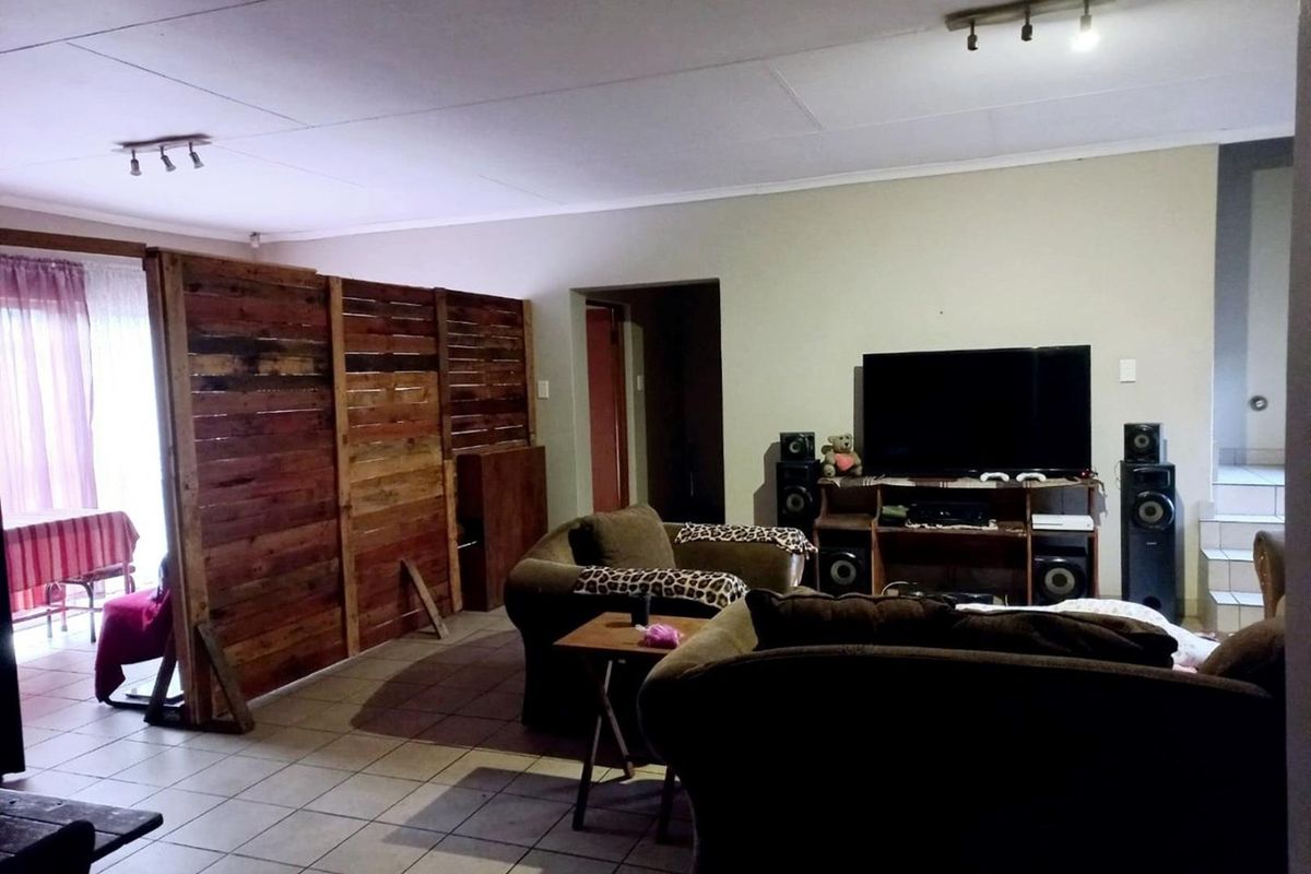 A living room area featuring tiled flooring and track lighting, currently partitioned with a wooden screen.