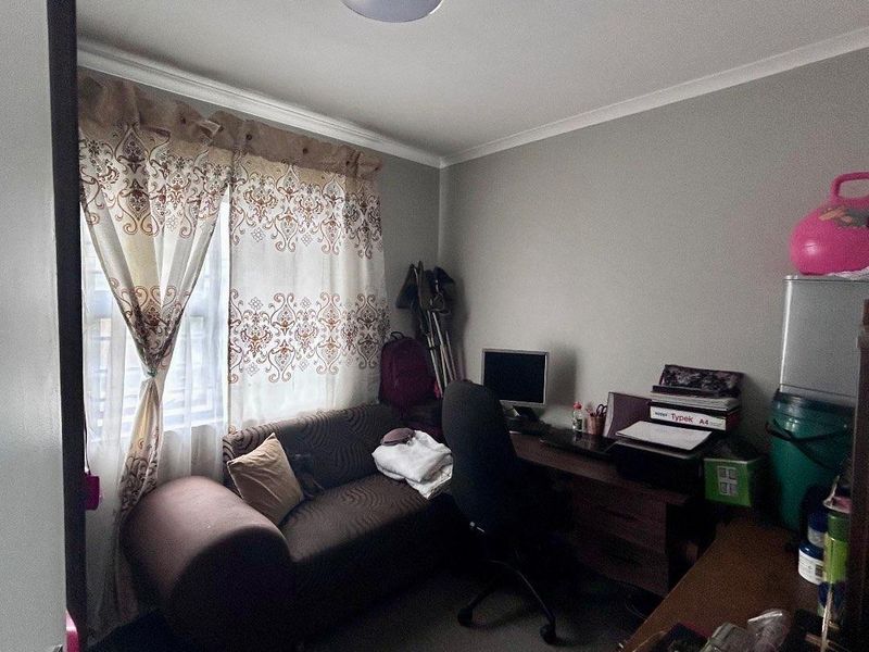 A compact bedroom featuring tiled flooring and a central ceiling light fixture, currently utilized as a multi-purpose study and living space.