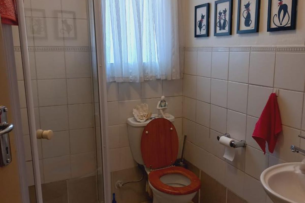A functional bathroom featuring a glass-enclosed shower, pedestal basin, and toilet with tiled walls and flooring.