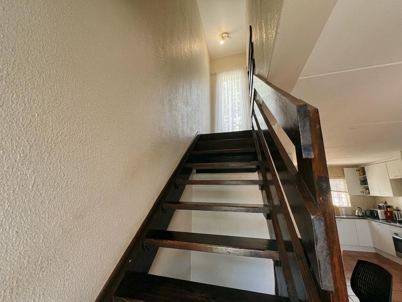 A wooden staircase leading to an upper level, featuring a simple handrail and neutral wall finishes, adjacent to an open-plan kitchen area.