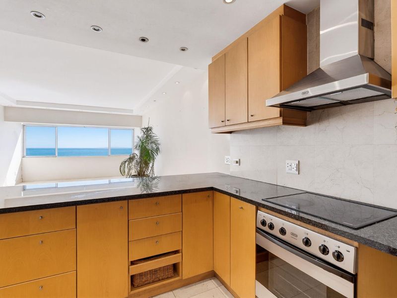 Open-plan kitchen featuring light wood cabinetry, granite countertops, and integrated appliances, flowing into a living area with expansive ocean views.