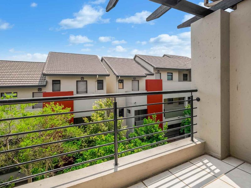 A clean, tiled balcony featuring a metal balustrade and a timber pergola, offering an elevated view of the surrounding apartment complex.