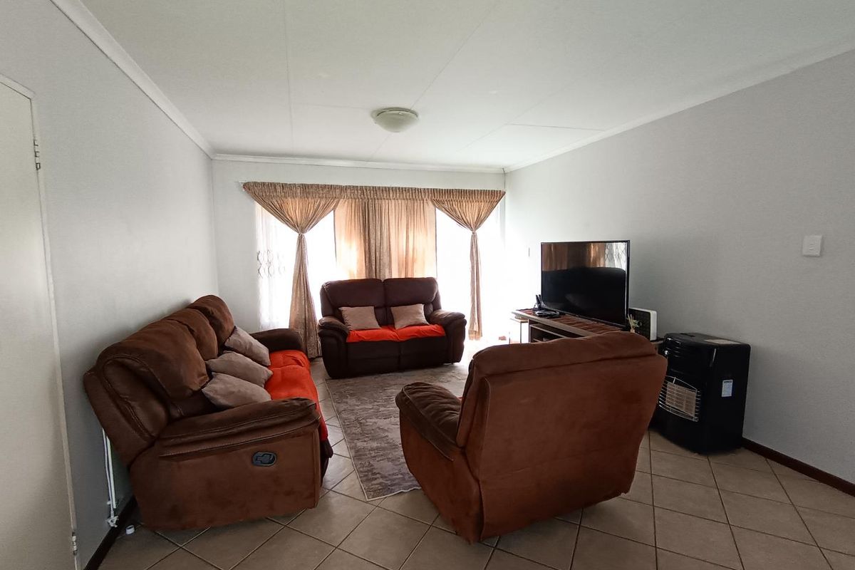 A spacious living room featuring neutral wall finishes, tiled flooring, and large windows that provide natural light.