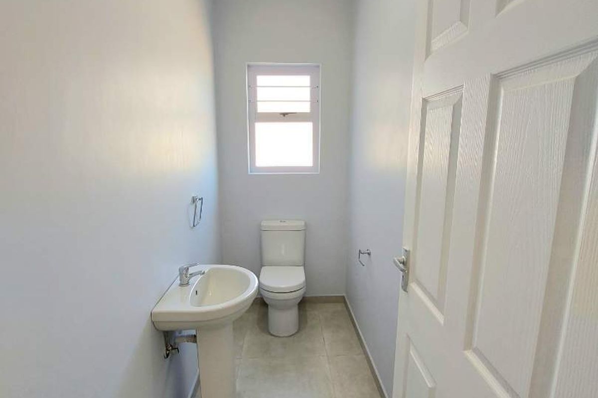 A clean and functional guest bathroom featuring a pedestal sink, toilet, tiled flooring, and neutral wall finishes.
