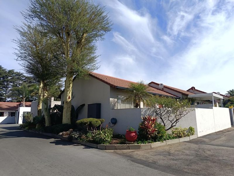 Front exterior view of the townhouse featuring a tiled roof, boundary wall, and established garden beds along the paved driveway.