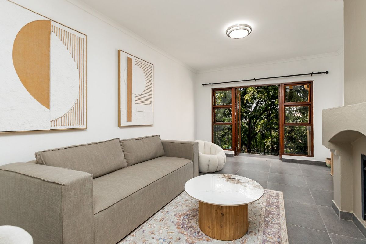 A bright living room featuring tiled flooring, a built-in fireplace, and wooden framed glass doors that open to a leafy outdoor view.