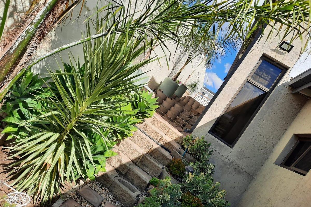 A side exterior view of the property featuring stone-stepped landscaping, established garden plants, and modern window fixtures along the building facade.