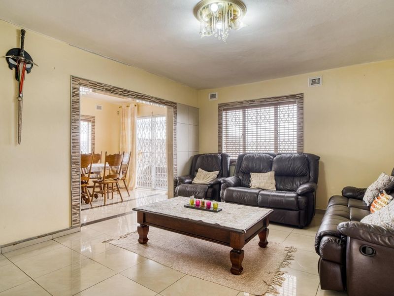 Spacious living room featuring tiled flooring, decorative lighting, and an open-plan transition to the adjacent dining area with security features.