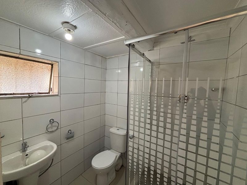 A functional bathroom featuring a pedestal basin, toilet, and a glass-enclosed shower with full-height wall tiling and a frosted window.