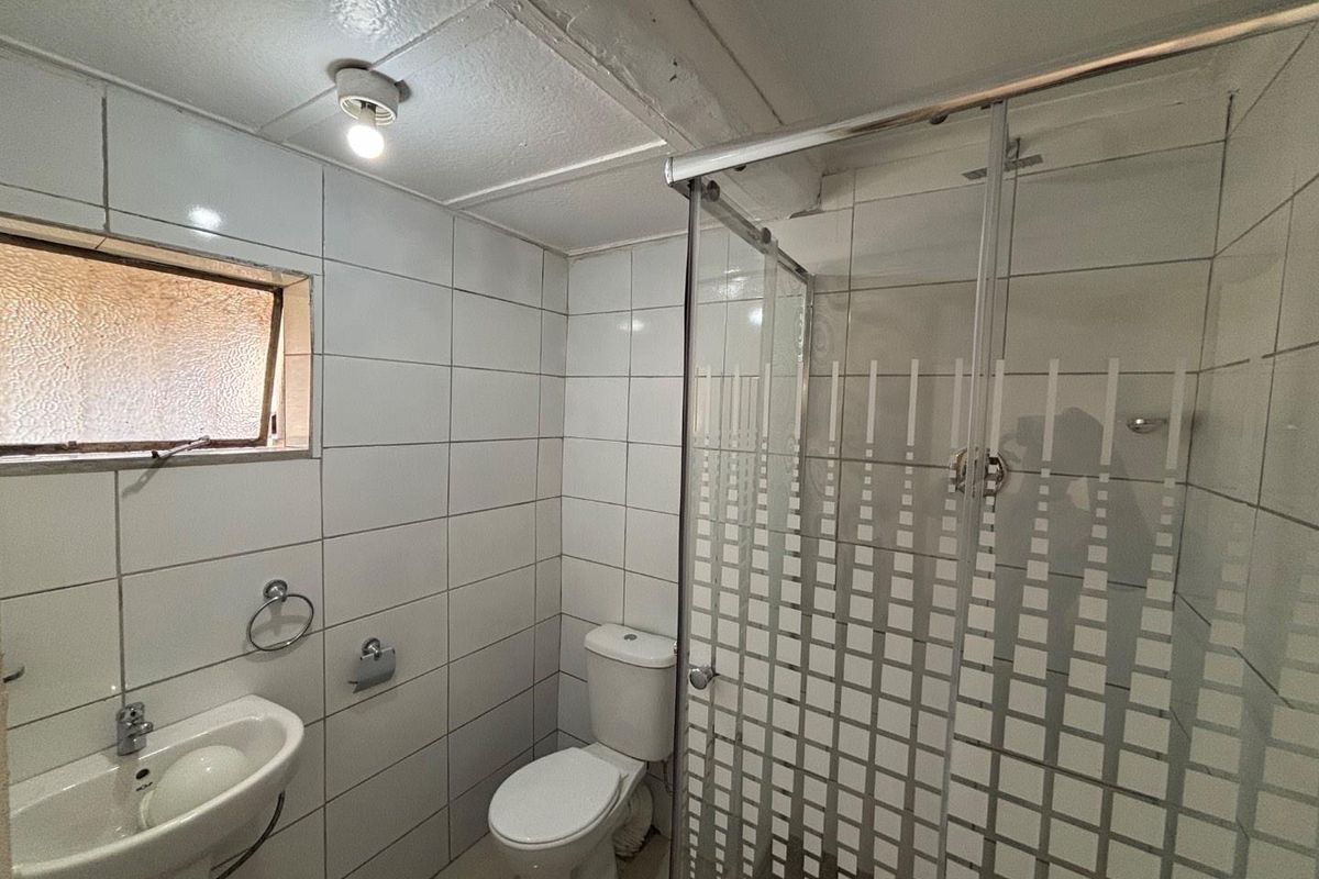 A functional bathroom featuring a pedestal basin, toilet, and a glass-enclosed shower with full-height wall tiling and a frosted window.