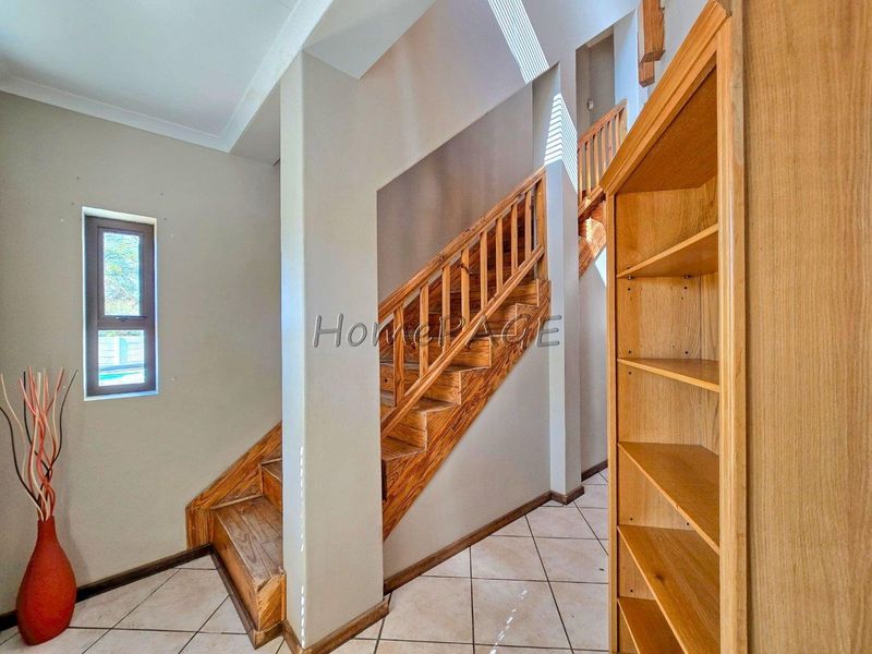 A bright hallway featuring a wooden staircase with a matching balustrade and neutral tiled flooring, providing access to the upper level of the home.