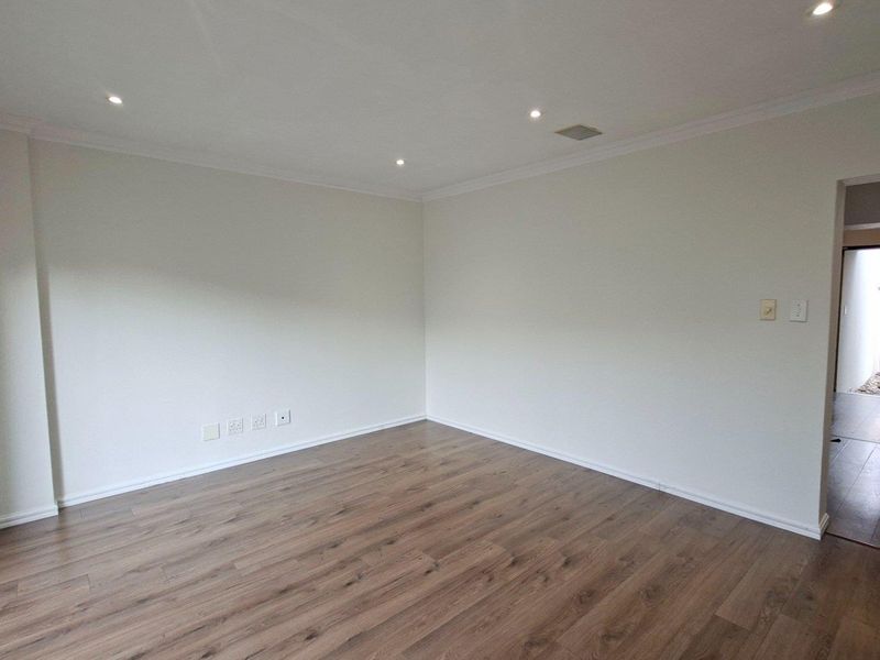 A bright, empty living area featuring modern laminate flooring, recessed downlighting, and neutral wall finishes, providing a versatile space for interior design.
