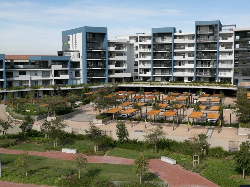 An elevated view of a modern apartment complex featuring landscaped gardens, paved pathways, and covered parking structures for residents.