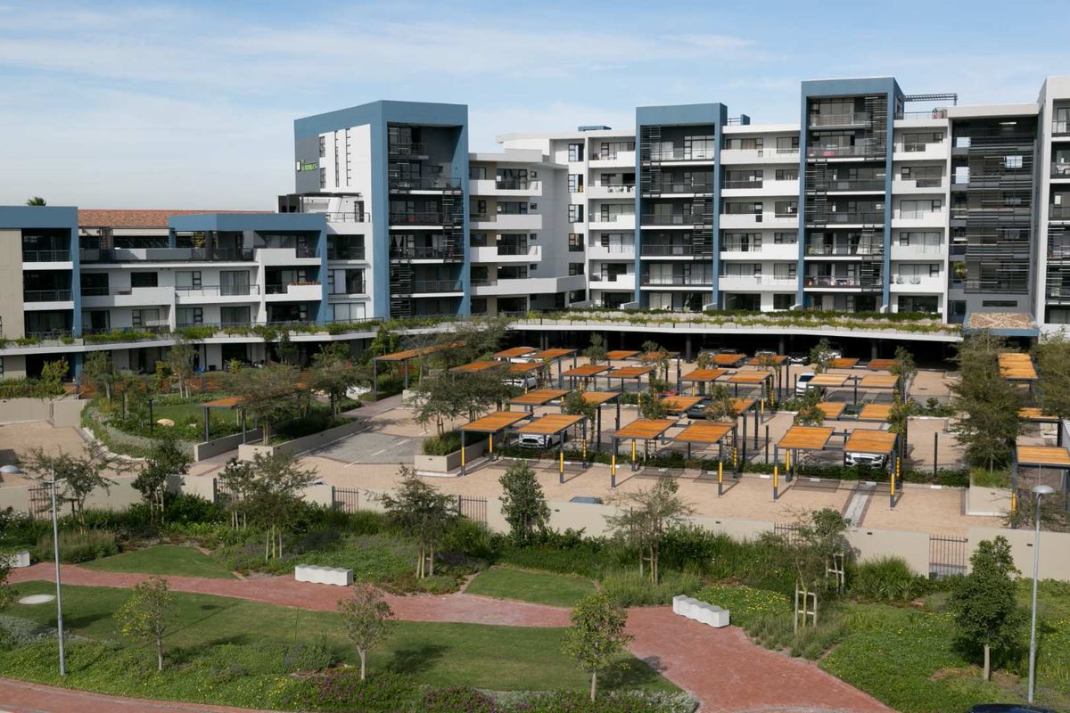An elevated view of a modern apartment complex featuring landscaped gardens, paved pathways, and covered parking structures for residents.