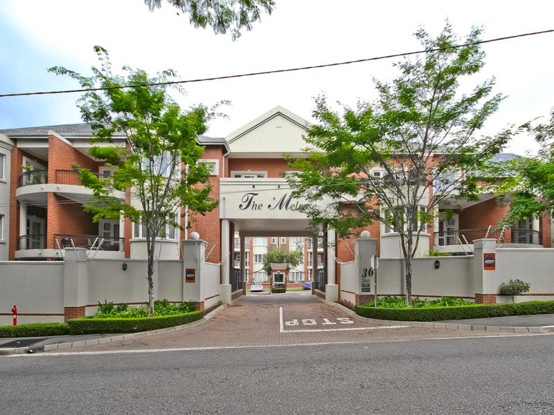Front elevation of The Melrose apartment complex, featuring a secure gated entrance, brick facade, and established landscaping.