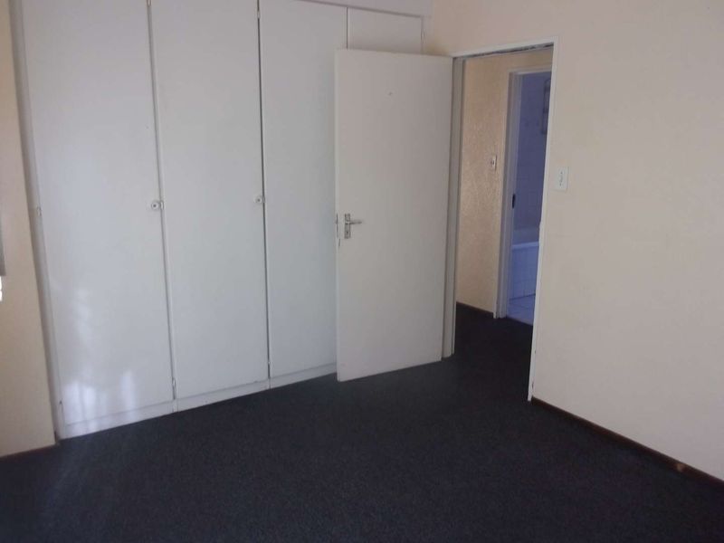 An empty bedroom featuring built-in cupboards, dark carpeting, and direct access to an adjacent bathroom.