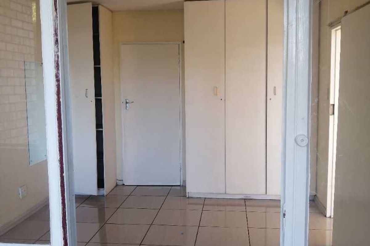 A vacant bedroom featuring built-in cupboards, tiled flooring, and a glass-paneled entrance door, offering a clean and functional living space.