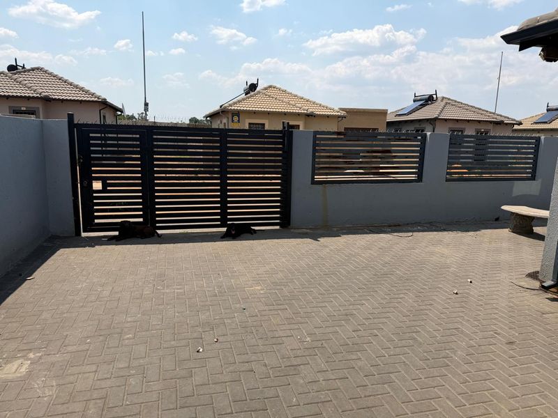 A paved rear courtyard area featuring a secure perimeter wall with integrated metal fencing and a gated entrance.