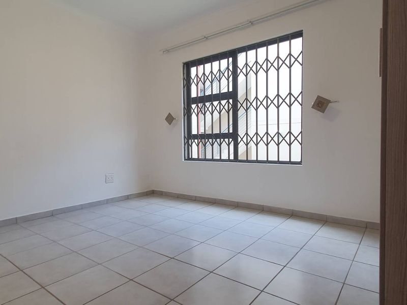 A clean, empty bedroom featuring neutral tiled flooring and a window fitted with a security gate.