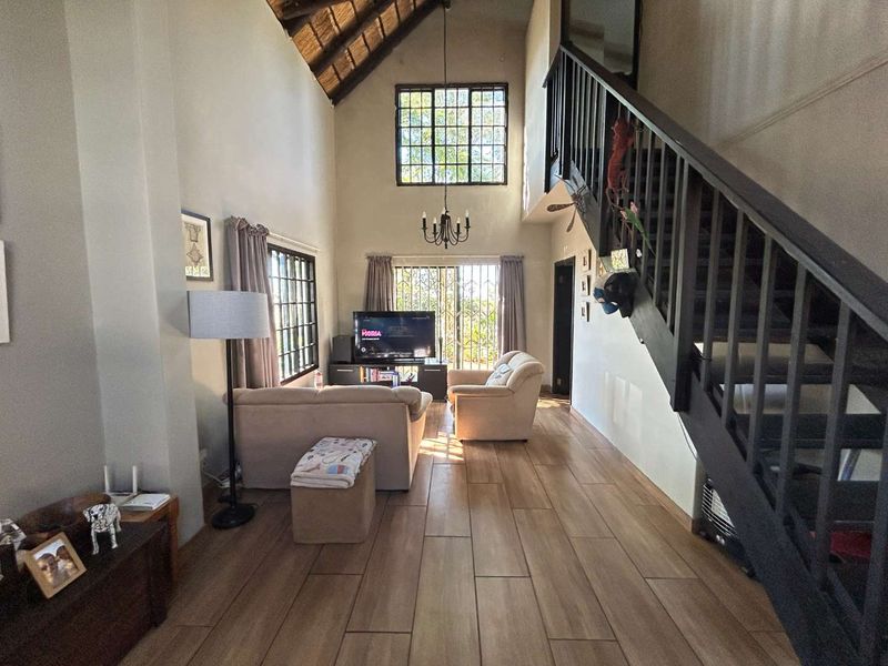 Spacious living room featuring a high vaulted thatch ceiling, timber staircase with balustrade, and modern wood-look tiled flooring with access to the outdoors.