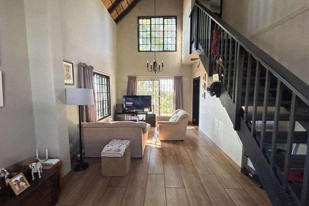 Spacious living room featuring a high vaulted thatch ceiling, timber staircase with balustrade, and modern wood-look tiled flooring with access to the outdoors.